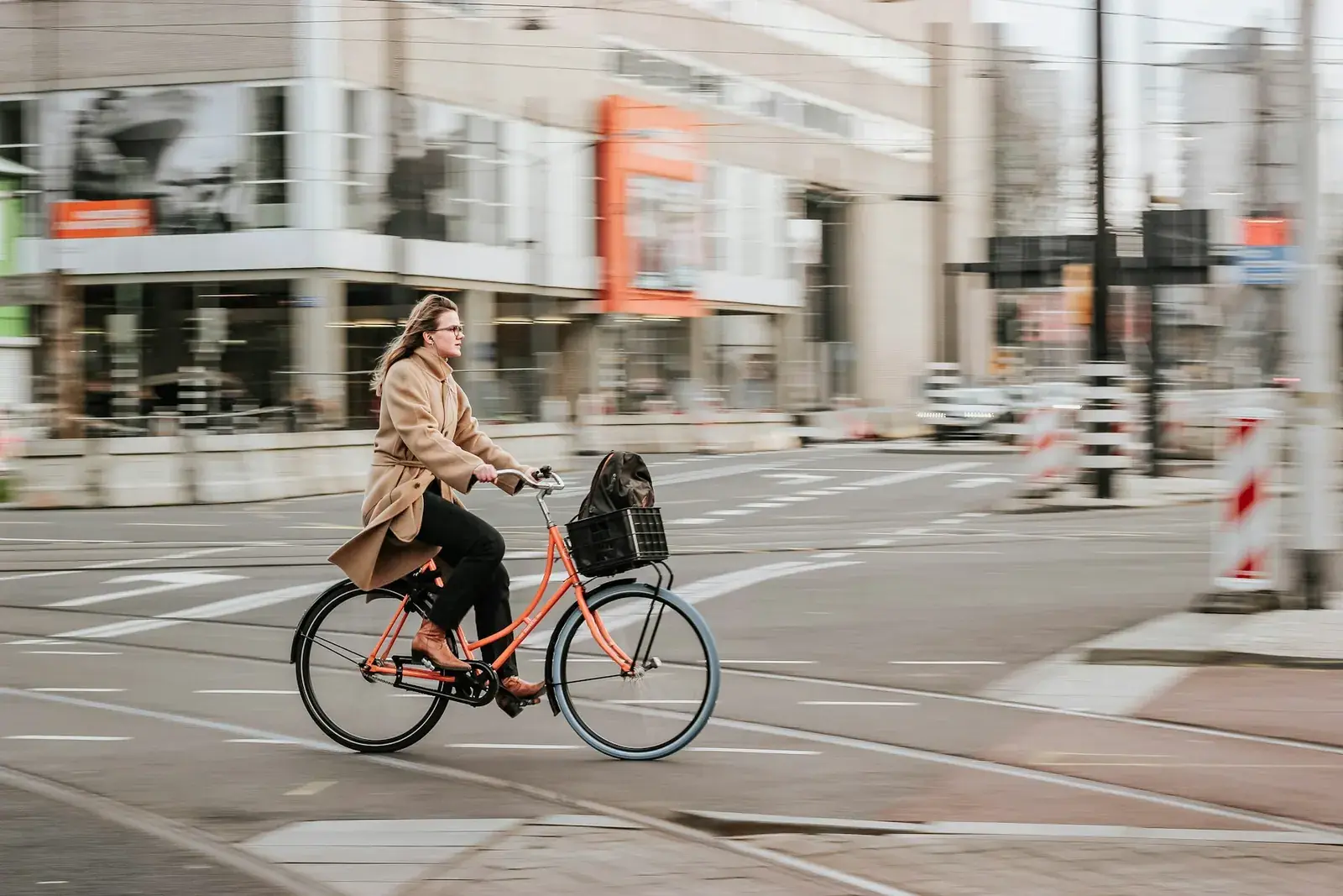 Een fietser in een beige jas rijdt door Rotterdam