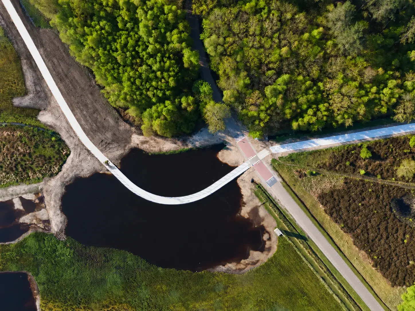 Van bovenaf: een fietser op een gebogen brug tussen water en groen op Texel