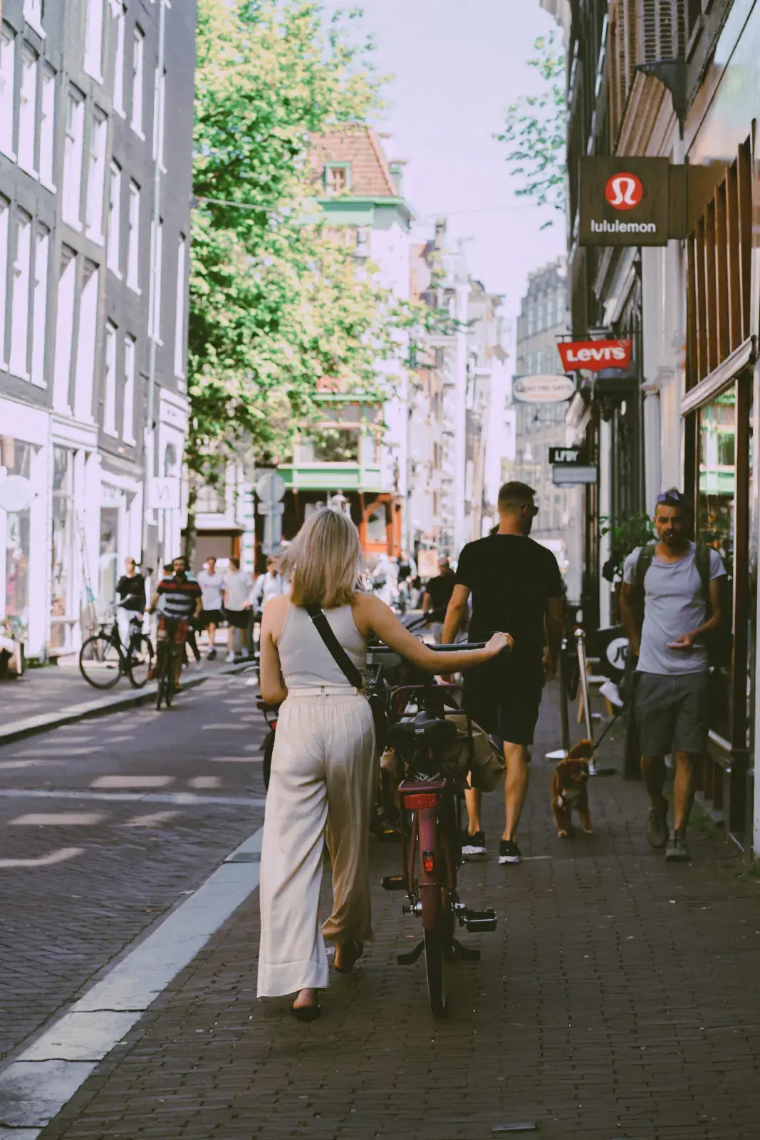 Een vrouw neemt haar fiets mee door een zonnige Amsterdamse straat
