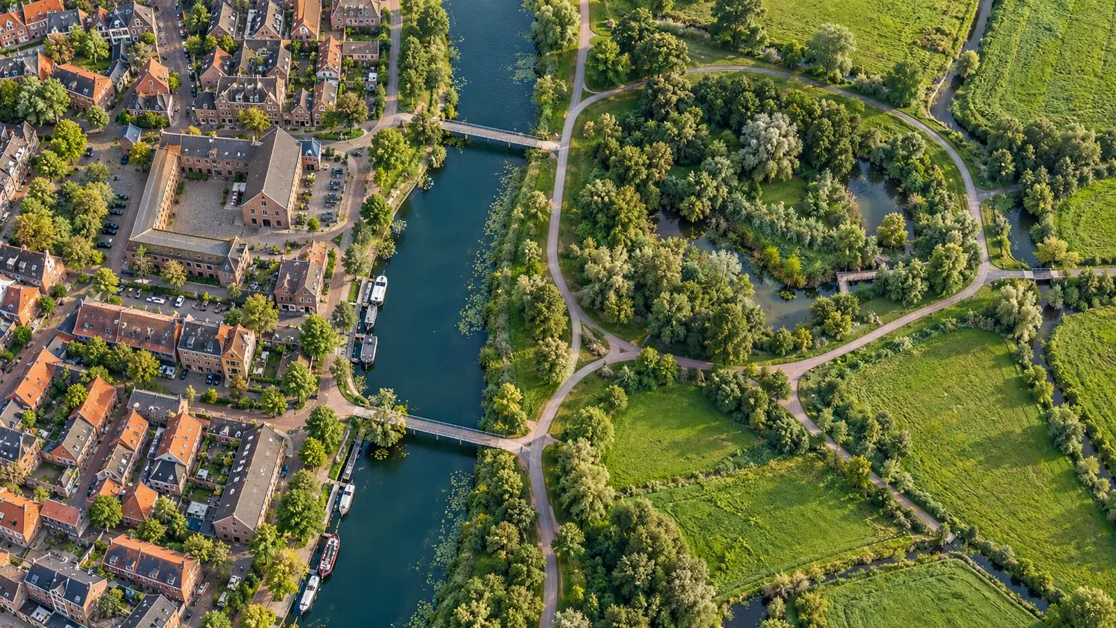 Een groen pad langs het water, tussen een woonbuurt en het open landschap